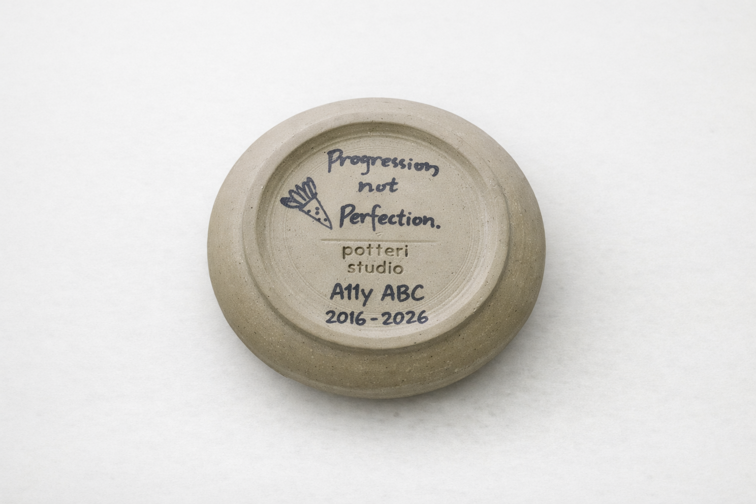 Base of coffee cup reads 'Progression not Perfection. A11y ABC 2016-2026, potteri studio'